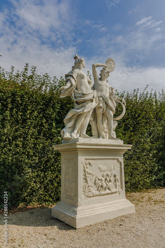 Classic white marble statue of woman with flute in green garden park. Ancient Roman or Greek woman stands on podium. the statue is surrounded by neatly trimmed bushes