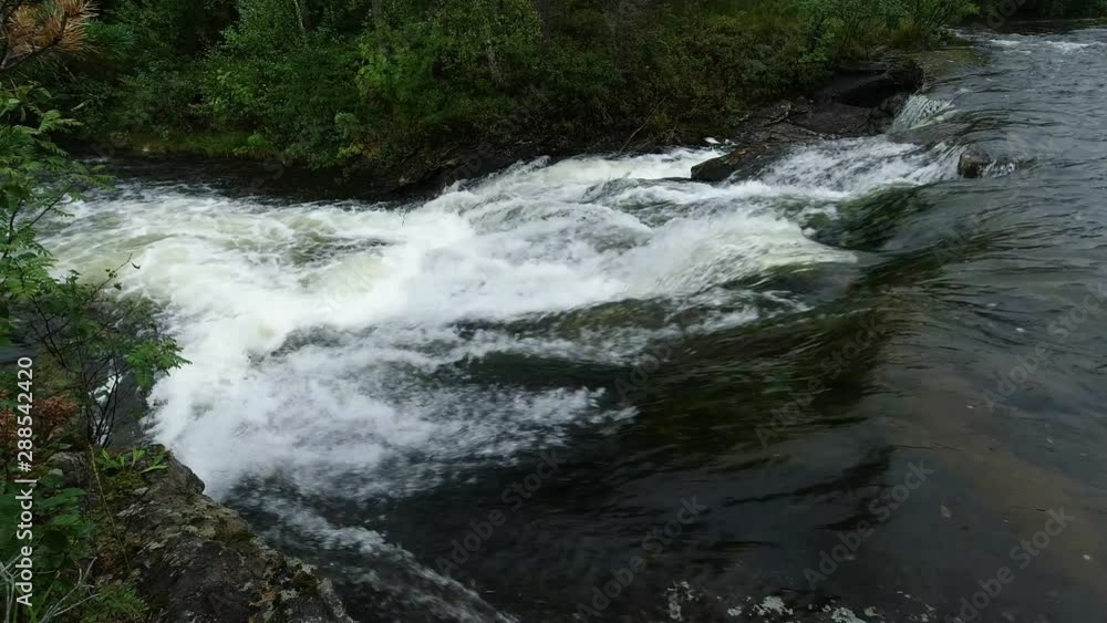 Stabile shot as water flowing by on a river, small waterfall, cascade causing the water to produce white foam. Stabile shot as water flowing by on a river, small waterfall, cascade causing the water to produce white foam.