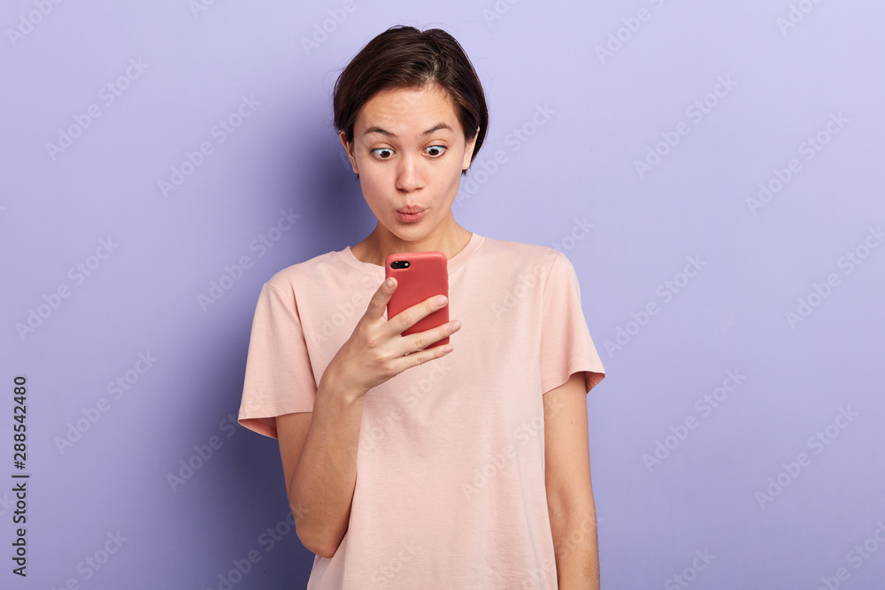 Closeup portrait of anxious nervous young girl looking at phone being shocked to receive bad news. Human emotion, reaction, expression. close up portrait. studio shot Closeup portrait of anxious nervous young girl looking at phone being shocked to receive bad news. Human emotion, reaction, expression. close up portrait. studio shot