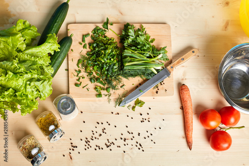 Fotografie Top view of wooden table with fresh raw cucumbers, lettuce, carrots, tomatoes, spices and chopped scallions on it, ingridients for cooking healthy and tasty meal