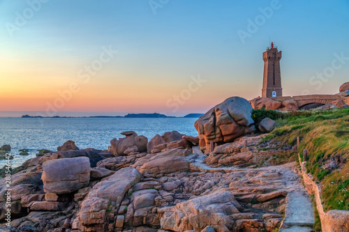 Sunset view of the Pink Granite Coast (Cote de Granite Rose) with Ploumanach Lighthouse (the Mean Ruz Lighthouse) in Perros-Guirec, textured boulders in the foreground. Brittany, France.