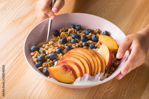 Bowl of granola with yogurt, peach slices and bluberry on a wooden table