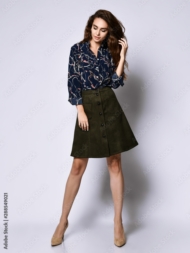 cheerful young woman posing in solitude, in a blue silk blouse with floral patterns, a dark short skirt with buttons and high-heeled shoes cheerful young woman posing in solitude, in a blue silk blouse with floral patterns, a dark short skirt with buttons and high-heeled shoes