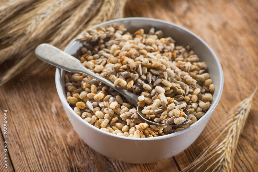 Tasty crispy granola in bowl with seeds and wheat on a wooden table Tasty crispy granola in bowl with seeds and wheat on a wooden table