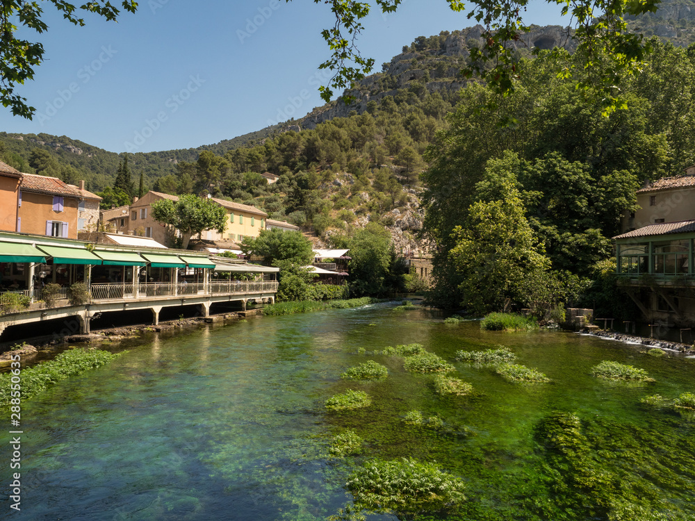 Fototapeta premium France, july 2019: Beautiful medieval village Fontaine de Vaucluse on the river shore. The poet Petrarch made it his preferred residence in the 14th century