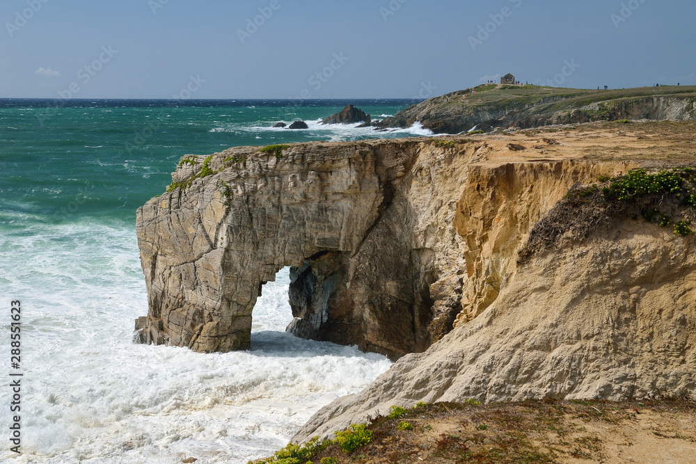Stormy weather with foamy ocean waves breaking against natural cliffs and stone arch 
