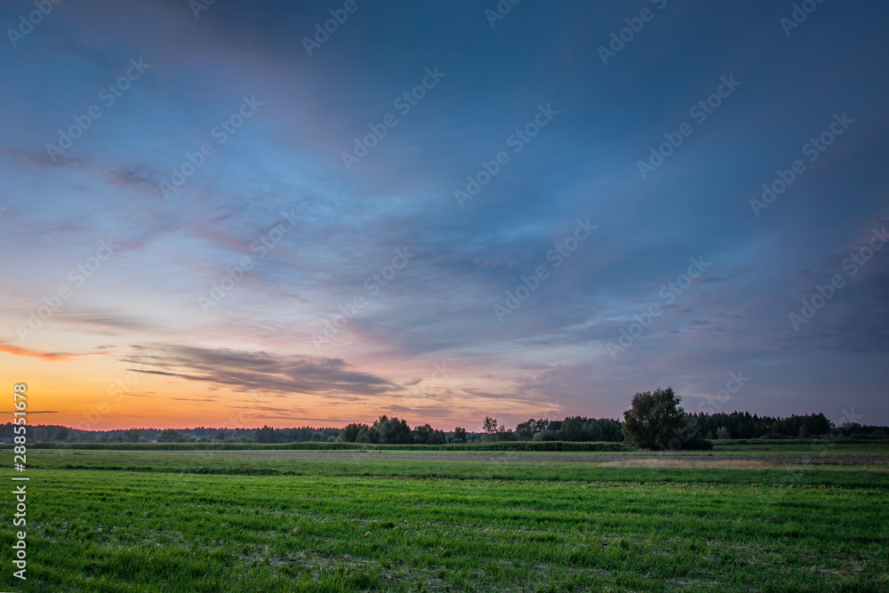 Colorful clouds after sunset, horizon and field