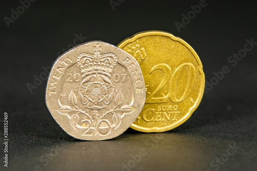 20 British pound pence and 20 euro cent coins with 20 pence in front on a black background photo