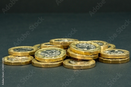 Flat pile of one and two British pound coins on a black background