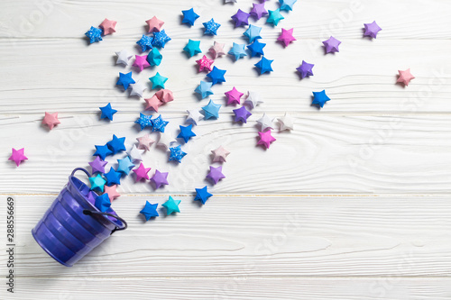 Coloful origami paper lucky stars folling out of the bucket on white wooden background. Greetings card