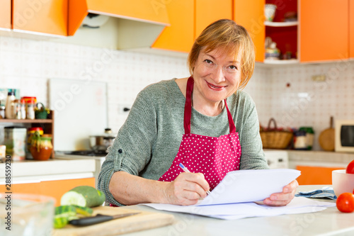 Mature housewife writes a recipe in the kitchen