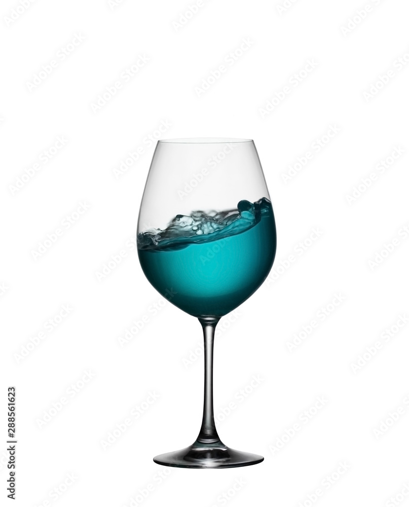 Splash of blue drink in glass on white isolated background. The splashing of blue water is like a sea wave in a glass. A splash of blue cocktail in a wine glass closeup. Splash of blue drink in glass on white isolated background. The splashing of blue water is like a sea wave in a glass. A splash of blue cocktail in a wine glass closeup.