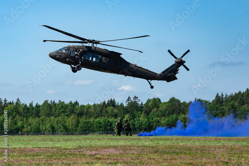 Landing of swedish military helicopter. Swedish Air Force. Military armed men with smoke bomb near forest under blue sky