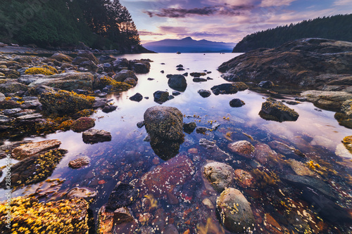 Brilliant sunset rocky beach scenes at sunset with mountains, sky and clouds lit up in early autumn.  Pacific North West Bowen Island British Columbia Canada close to Vancouver.