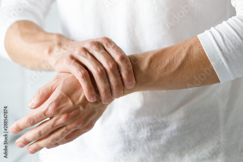 Closeup of male arms holding her painful wrist caused by prolonged work on the computer, laptop. Carpal tunnel syndrome, arthritis, neurological disease concept. Numbness of the hand photo