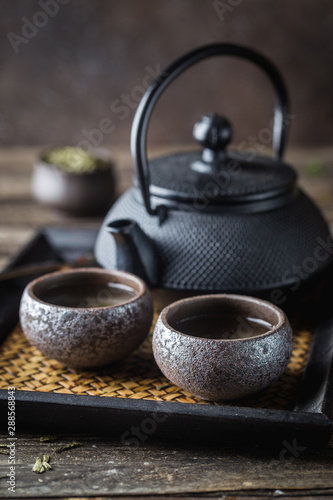 Still-life of japanese healthy green tea in a small cups and teapot over dark background