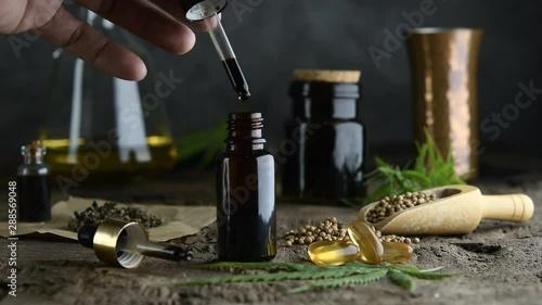 hemp essential oil in small glass bottle. container with cannabis leaves and cannabis seeds on wooden.