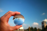 glass crystal ball in hand and city reflection on summer sunny day against beatiful blue cloudy sky