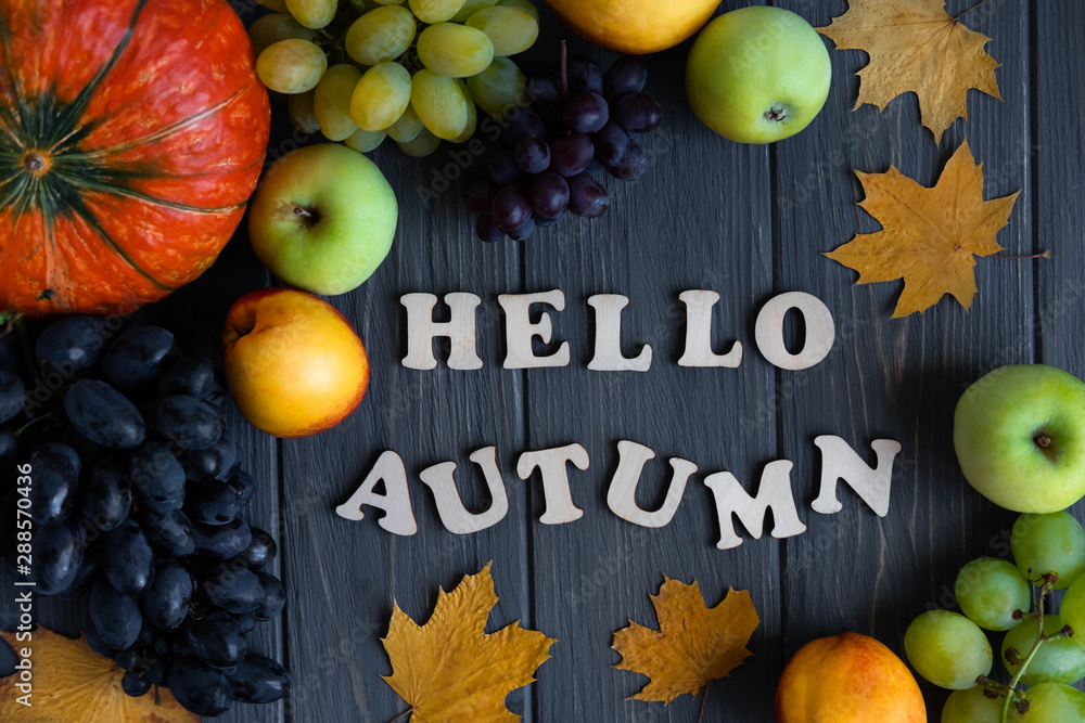 Lettering Hello Autumn from wooden letters. Autumn banner with pumpkin, grapes, apples, nectarine on a gray wooden background. Autumn harvest on the farm, garden
