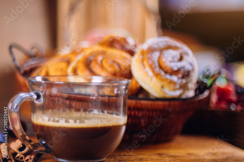 Black coffee and cinnamon buns on wooden table.