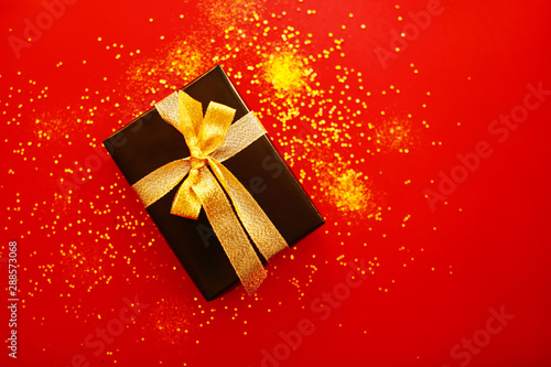 New Year's gift on a bright red background with gold sparkles. Box with gold ribbon. © Vera