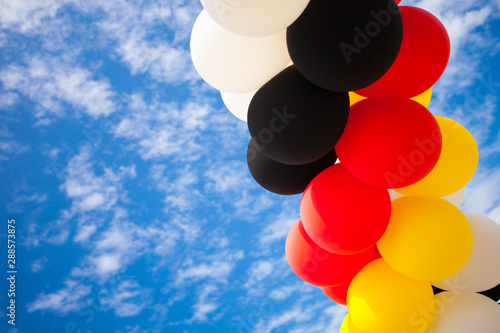 Balloons - Colors of the German National Flag (black, red, yellow)  - outdoors against blue Sky with white Clouds - Symbol for Festivity or Celebration