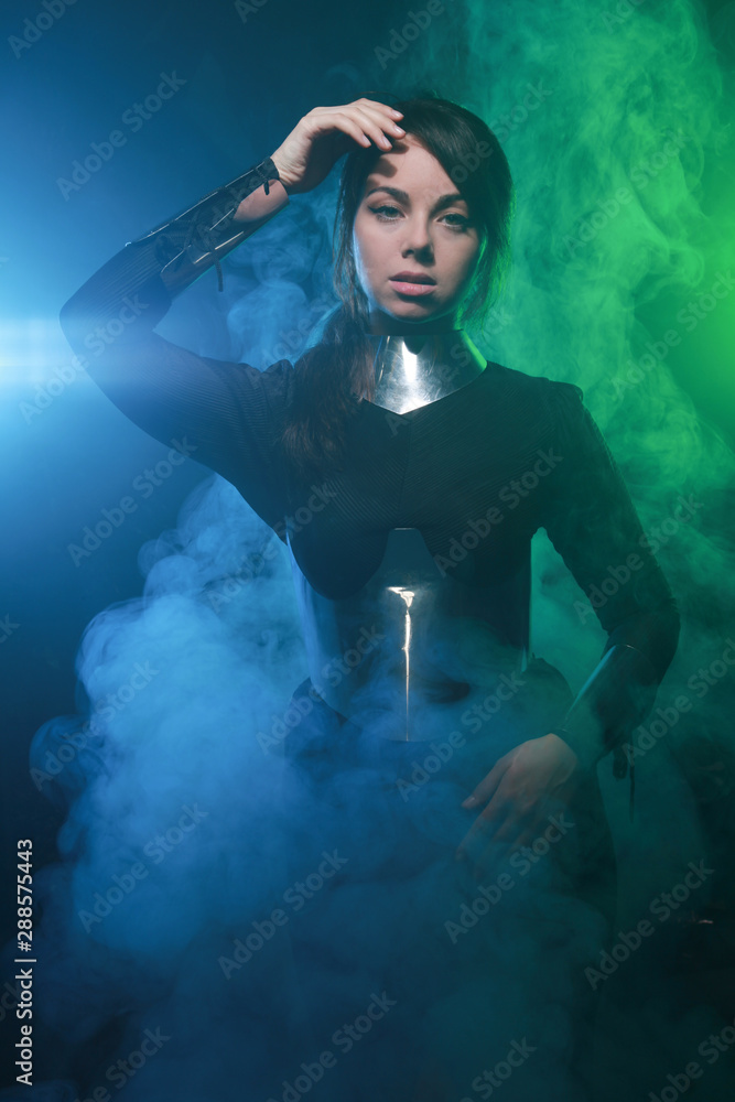 futuristic fashion model wearing black and silver clothes and standing in the colorful blue and green smoke