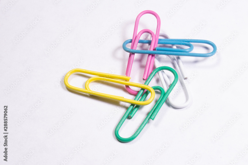 Several colored metal clips lying on a white matte surface Several colored metal clips lying on a white matte surface