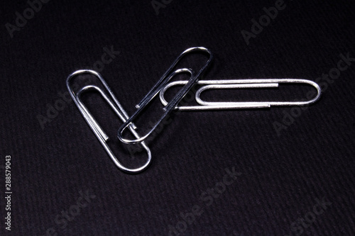 Three shiny metal clips lying on a matte black surface