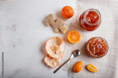 Tangerine and kumquat jam in a glass jar on white wooden  background.