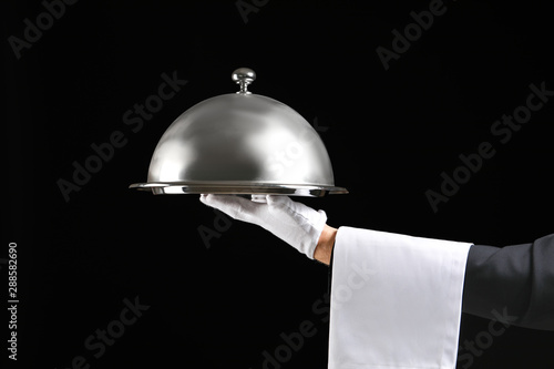 Hand of waiter with tray and cloche on dark background photo