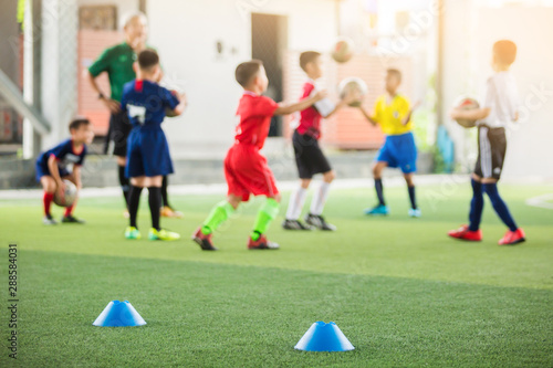 selective focus to marker cones are soccer training equipment on green artificial turf with blurry kid players training background. material for training class of football academy.