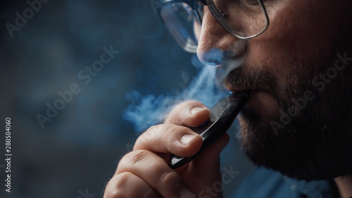 Man smokes new Vape Pod System, inhales and exhales vapor of electronic cigarette, vaping concept photo