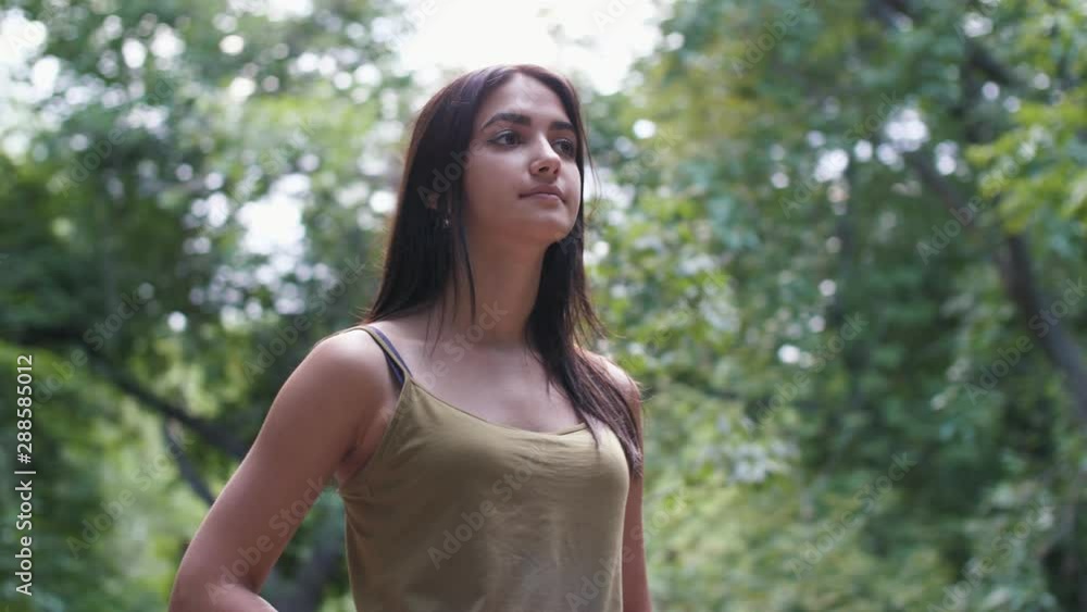 Cheery girl standing in a green alley and looking up in summer in slow motion Cheery girl standing in a green alley and looking up in summer in slow motion