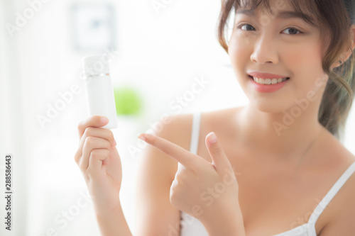Beautiful portrait young asian woman holding and pointing presenting cream or lotion product  beauty asia girl show cosmetic makeup and moisturizing for skin care  healthy and wellness concept.