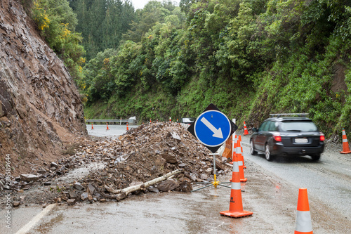 Photos Automobile car driving past rockflall, rocks, landslide debris, traffic cones and warning signs on roadway highway