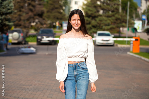 Young beautiful brunette woman in jeans and white blouse walking in summer street © Andrey_Arkusha