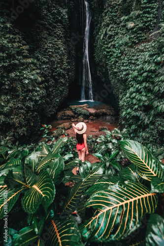 Traveling young woman with tropical rainforest in Bali enjoying life at beautiful Lake Lake waterfall. photo