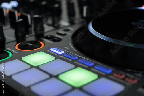 Close up DJ mixer player and sound console for house music party. DJ controller for mixing music and colorful light in nightclub. Disc jockey panel and mixing deck at dance party