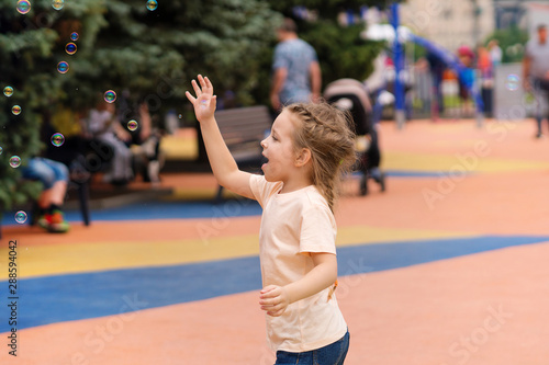 Carefree time in the playground. Cute little girl catches soap bubbles. Happy childhood, lifestyle concept photo