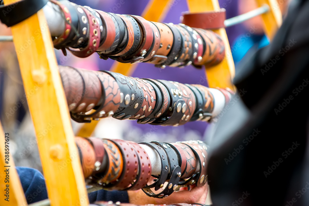 Beautiful leather bracelets of different colors with embossed and rivets hang on the stand at the seasonal fair of masters.