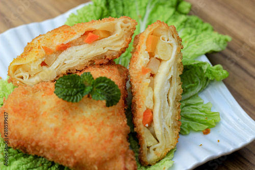 fried triangle risoles on a saucer with vegetables and chicken in it