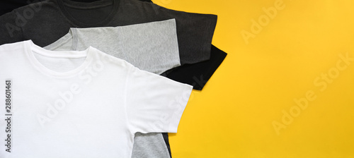 top view stack of black, grey and white (monochrome) t-shirt on yellow background with copy space, flat lay