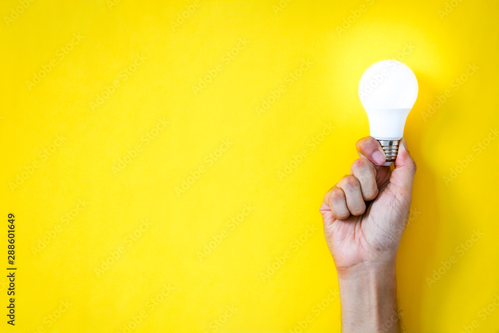 man's hand holding LED light bulb over yellow  color background with copy space, flat lay, concept of ideas - obrazy, fototapety, plakaty 