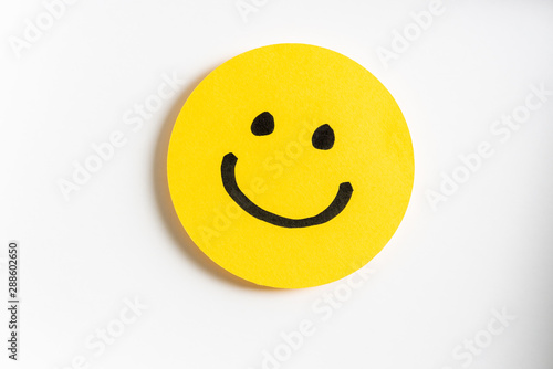 Drawing of a happy smiling emoticon on a yellow paper and white background.