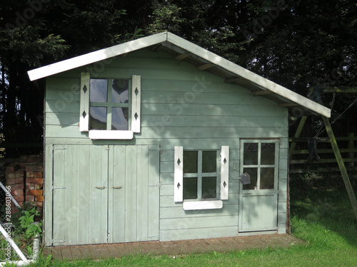 Green pastel colored wooden playhouse in shaded garden