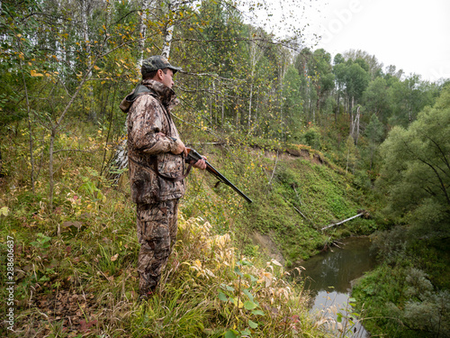 A hunter with a gun tracks the game in the autumn forest.