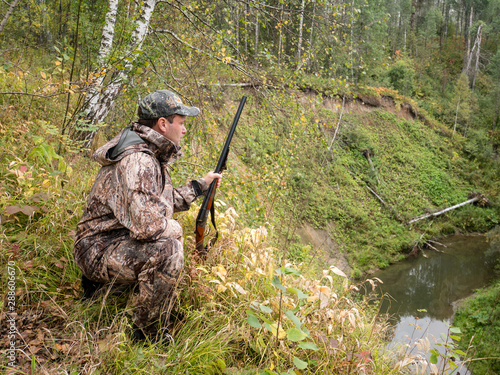 A hunter with a gun tracks the game in the autumn forest.