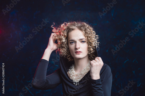 Photos Handsome androgynous young man in the image of a woman passionately posing against a dark background, putting a hood over her face