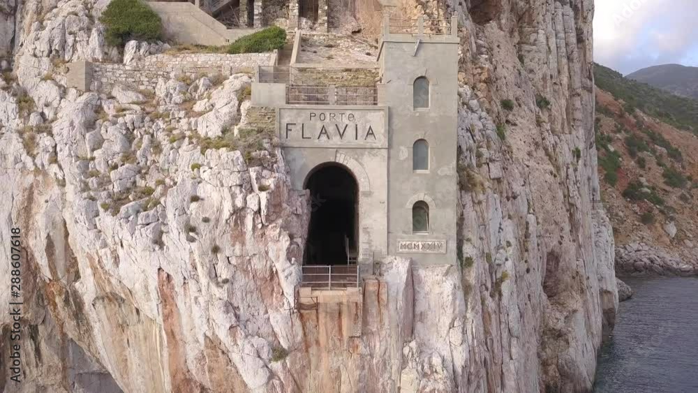 Drone shot of Porto Flavia an abandoned mineral storage pier in the coast of Sardinia in Italy.The shot is moving from the inside to the outside of the storage tunnel. Drone shot of Porto Flavia an abandoned mineral storage pier in the coast of Sardinia in Italy.The shot is moving from the inside to the outside of the storage tunnel.